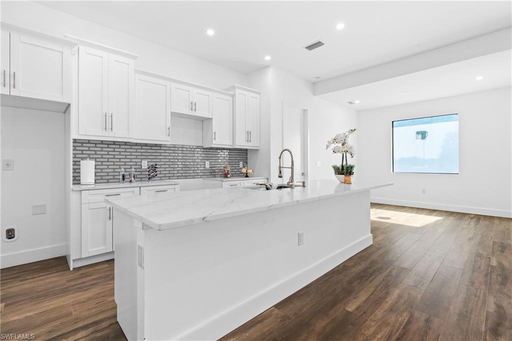 Contemporary kitchen featuring a large central island with a light-toned countertop, white cabinetry with silver-toned hardware, a distinctive gray subway tile backsplash, and recessed lighting