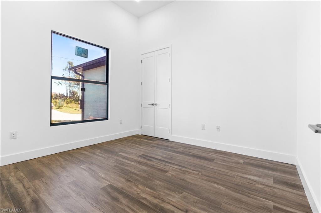 Room featuring wood-finish flooring, a large black-framed window, bright white walls, and a white double door