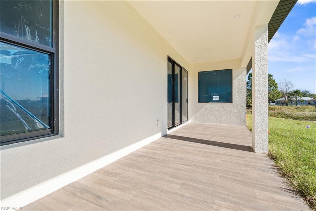 Expansive covered patio featuring wood-look tile flooring, textured stucco walls, black-framed sliding glass doors, and a recessed lighting fixture