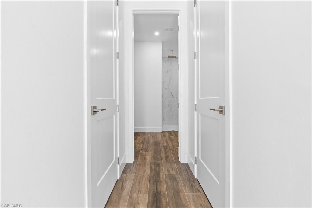 Hallway featuring wood-finish flooring, white paneled doors with brushed nickel hardware, and recessed lighting