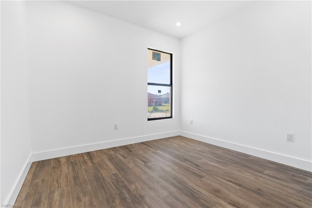 Room featuring wood-finish flooring, white walls, white baseboards, a black-framed vertical window, and recessed ceiling lighting