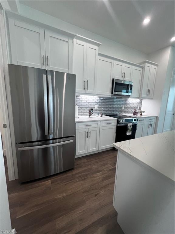Modern kitchen featuring wood-finish flooring, white cabinetry, stainless steel appliances, a subway tile backsplash, and light-toned countertops