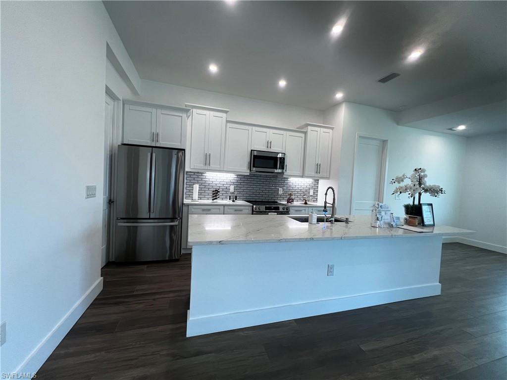 Contemporary kitchen featuring a large island with a surface, stainless steel appliances, white cabinetry, a tiled backsplash, and recessed lighting