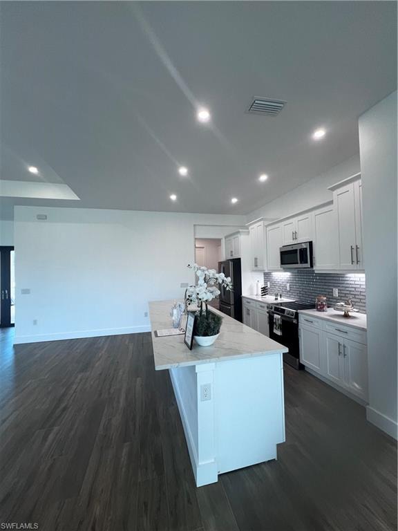 Kitchen featuring a central island with a light-toned countertop, white cabinetry with silver-toned hardware, a gray subway tile backsplash, recessed lighting, and dark wood-finish flooring