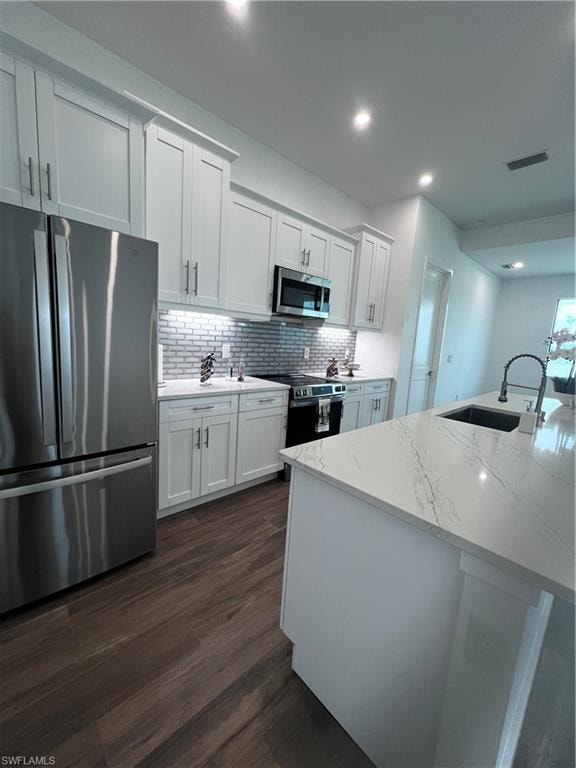 Modern kitchen featuring white shaker cabinetry, stainless steel appliances, wood-finish flooring, a mosaic tile backsplash, and a large island with a light-toned countertop