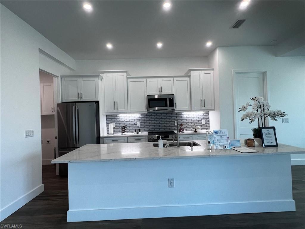 Kitchen featuring a large island with a stone countertop, white shaker cabinetry, stainless steel appliances, and a subway tile backsplash
