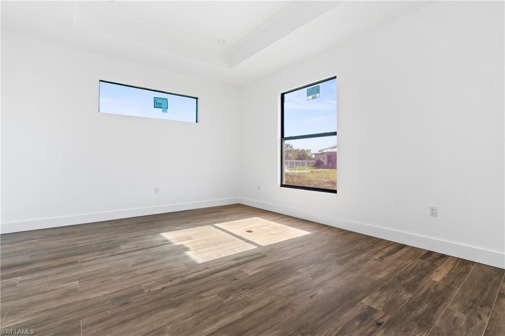 Spacious room featuring wood-finish flooring, white walls, and a tray ceiling