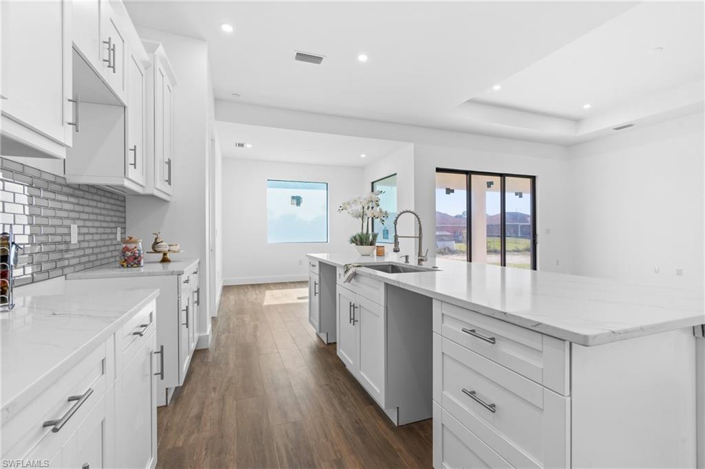 Modern kitchen featuring white shaker cabinetry, an expansive island with a rectangular sink, light-toned countertops, and a subway tile backsplash