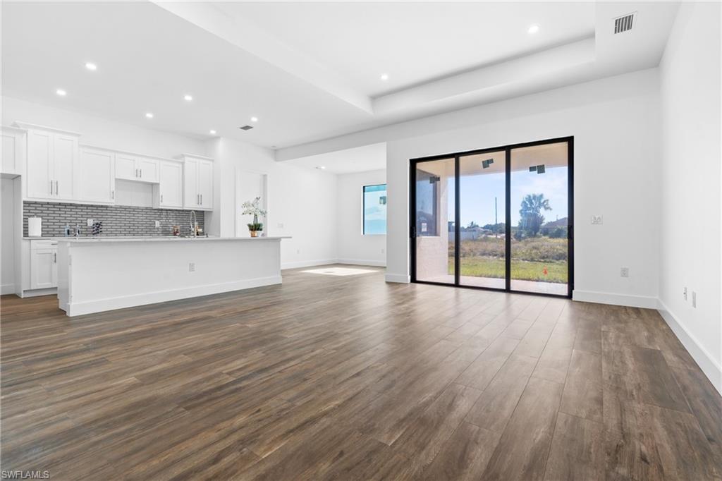 Open-concept living area with wood-finish flooring, a contemporary kitchen featuring white cabinetry, a tiled backsplash, and an island