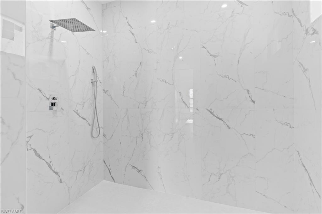 Walk-in shower with large-format white tile featuring grey veining, a rain showerhead, and a handheld shower fixture