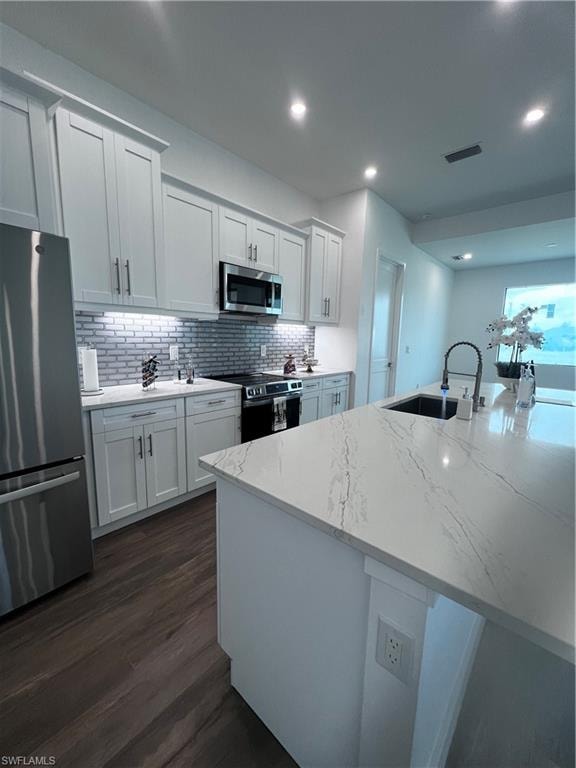 Modern kitchen featuring light gray shaker cabinetry, stainless steel appliances, a white subway tile backsplash, and wood-finish flooring