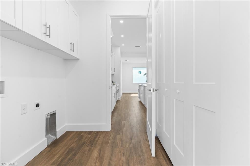 Laundry area featuring white cabinetry with silver hardware, durable wood-finish flooring, and white bifold doors