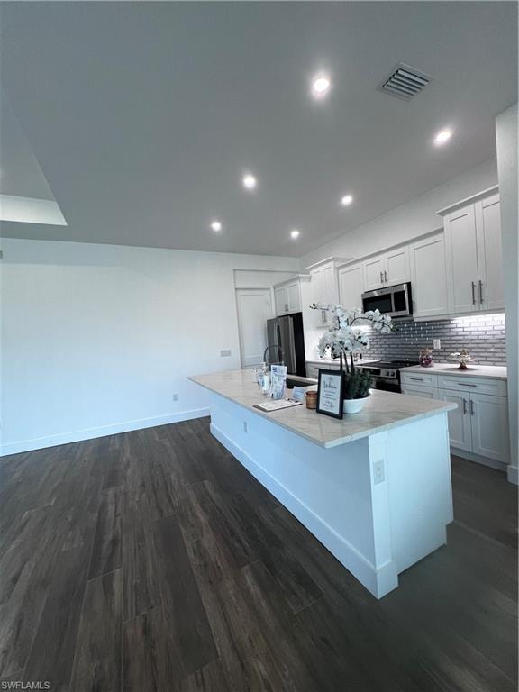 Kitchen island with light-toned countertop, dark wood-finish flooring, recessed lighting, and white cabinetry