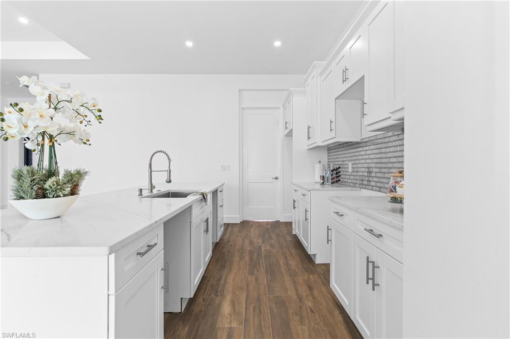 Contemporary kitchen featuring white cabinetry, light countertops, wood-finish flooring, a stainless steel sink with a gooseneck faucet, and a subway tile backsplash
