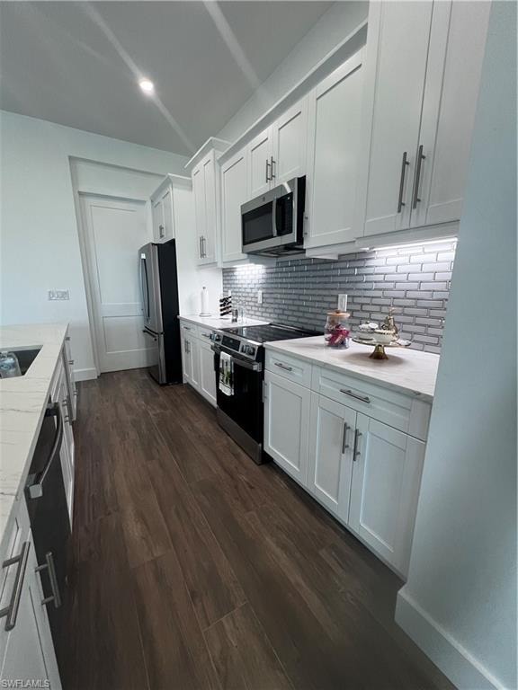 Modern kitchen featuring white shaker cabinetry, stainless steel appliances, a subway tile backsplash, light stone countertops, and wood-finish flooring