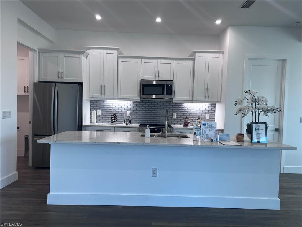 Contemporary kitchen featuring a large island with a light-colored countertop, white shaker-style cabinetry, stainless steel appliances, a subway tile backsplash, and recessed lighting