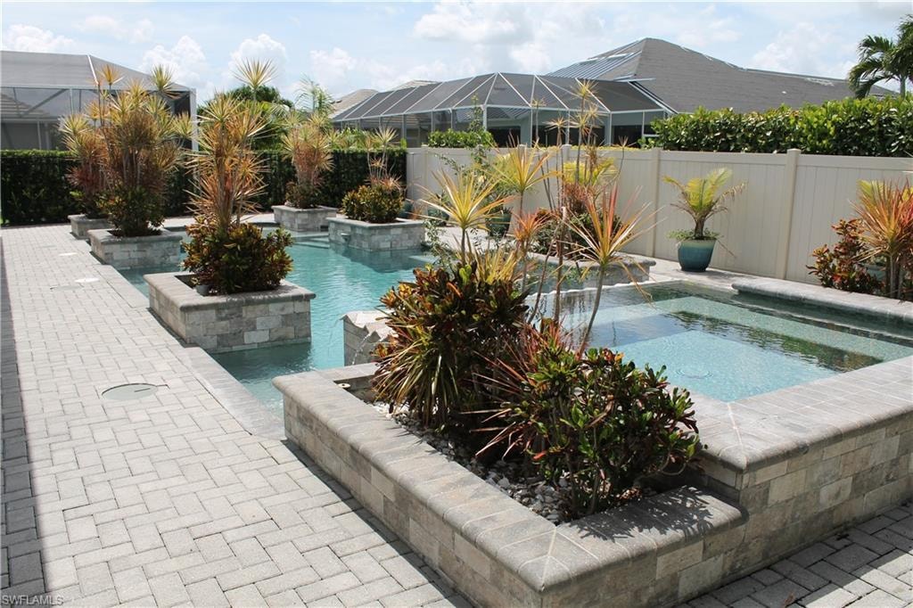 Outdoor pool with integrated planter boxes featuring mature tropical plantings, a paver patio, and a privacy fence