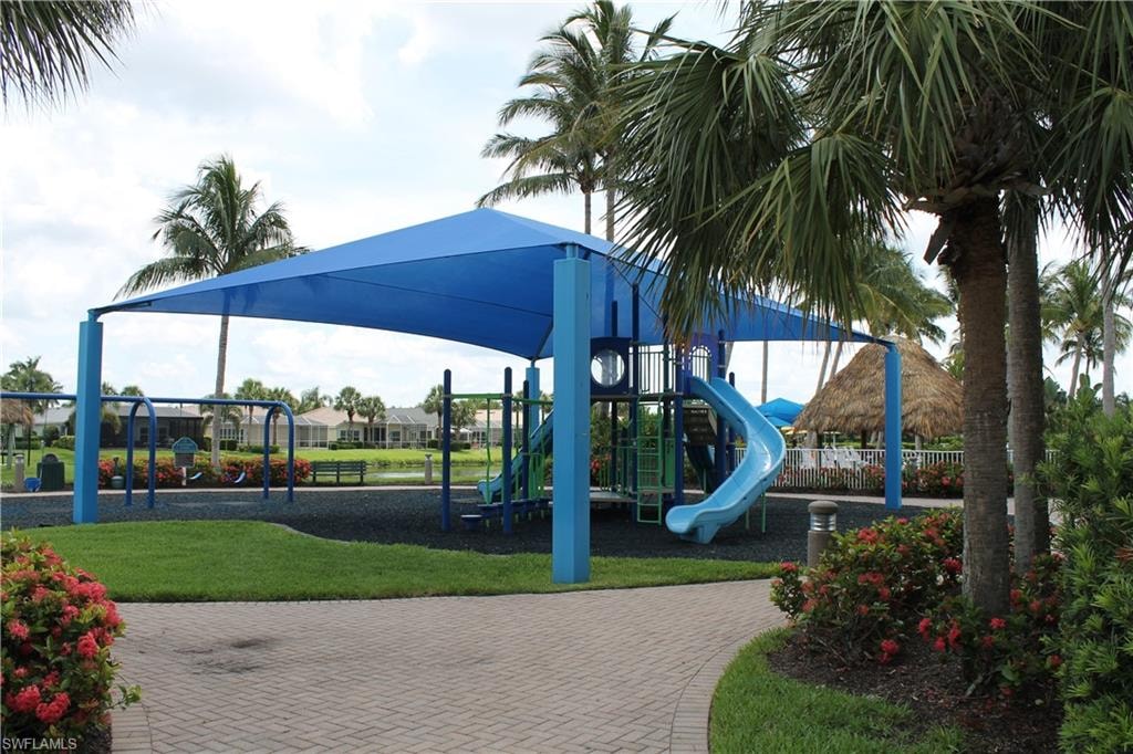 Shaded playground featuring multiple slides and swings, surrounded by lush green landscaping and mature palm trees