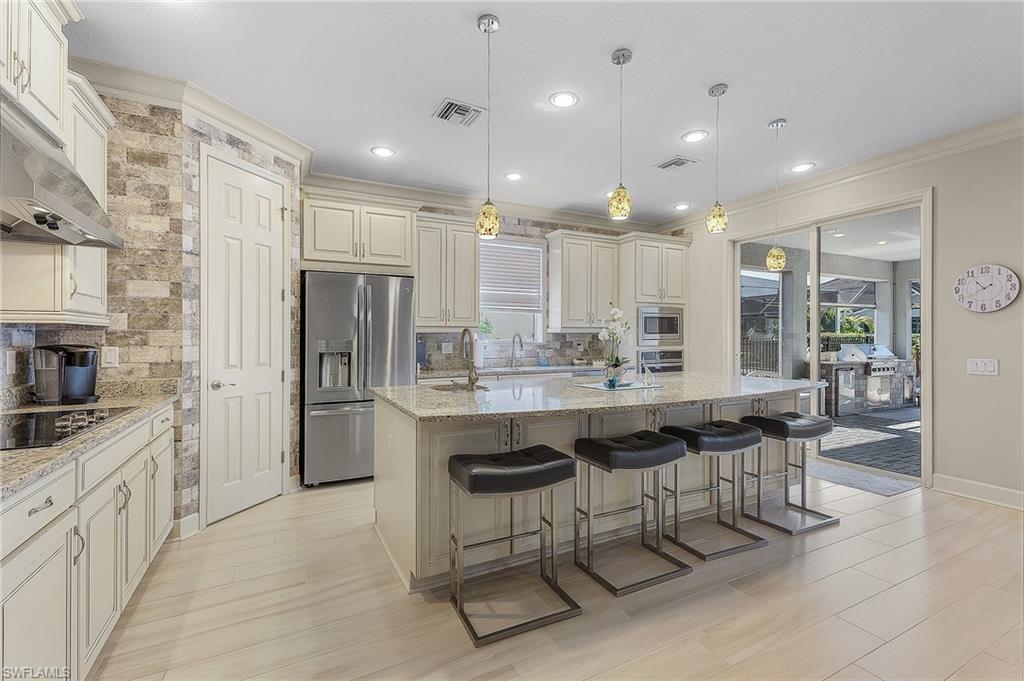 Spacious kitchen featuring an expansive central island with seating, pendant lighting, stainless steel appliances, and light-toned cabinetry