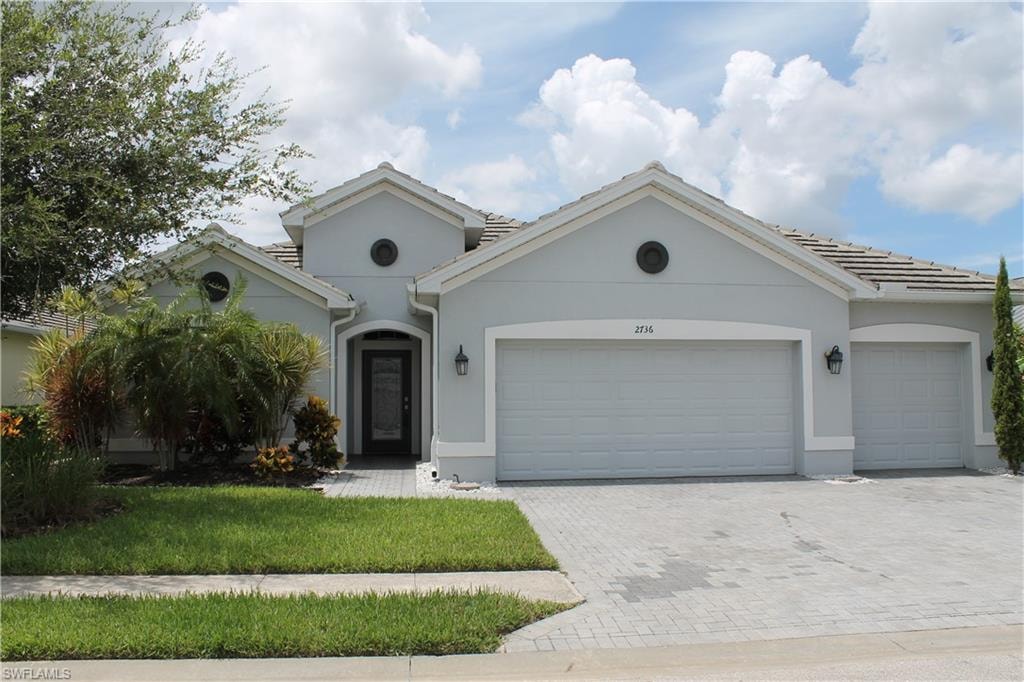 Stucco exterior with a tiled roof, featuring a paver driveway, two-car garage, single entry door, and manicured landscaping