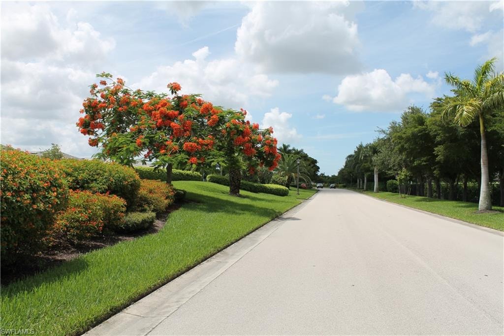 Paved road bordered by lush green lawns and a variety of mature trees and shrubs