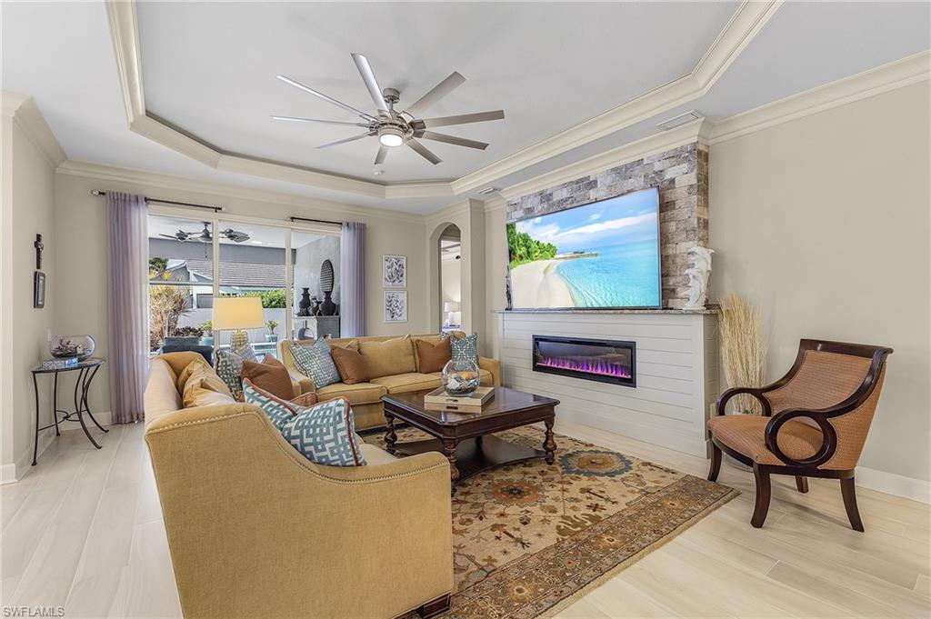 Tray ceiling with a ceiling fan, stone-accented media wall with an integrated electric fireplace, wood-finish flooring, and sliding glass doors to the exterior