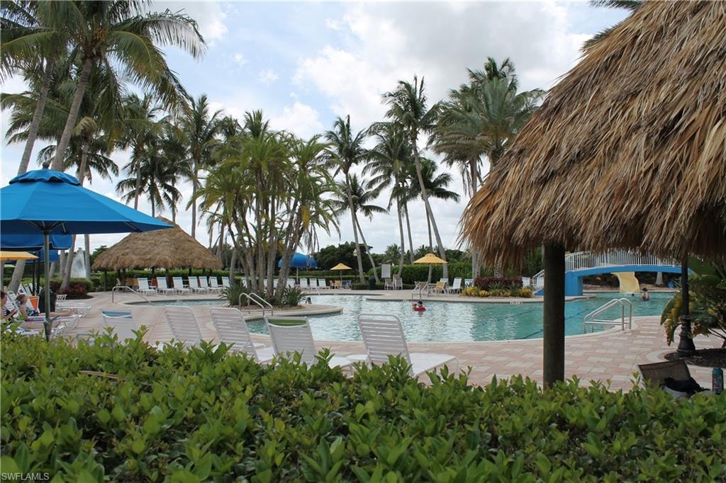 Expansive aquatic amenity featuring multiple pools, a thatch-roofed structure, and an abundance of mature palm trees