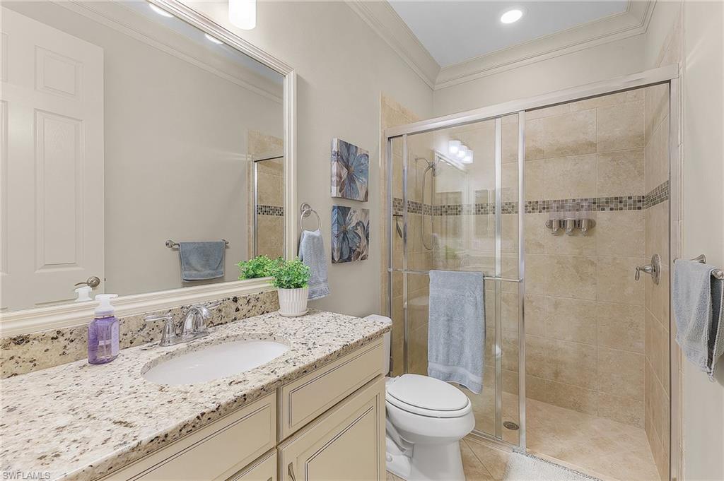 Bathroom featuring a glass-enclosed shower with tile surround, a single vanity with stone countertop, and a built-in mirror