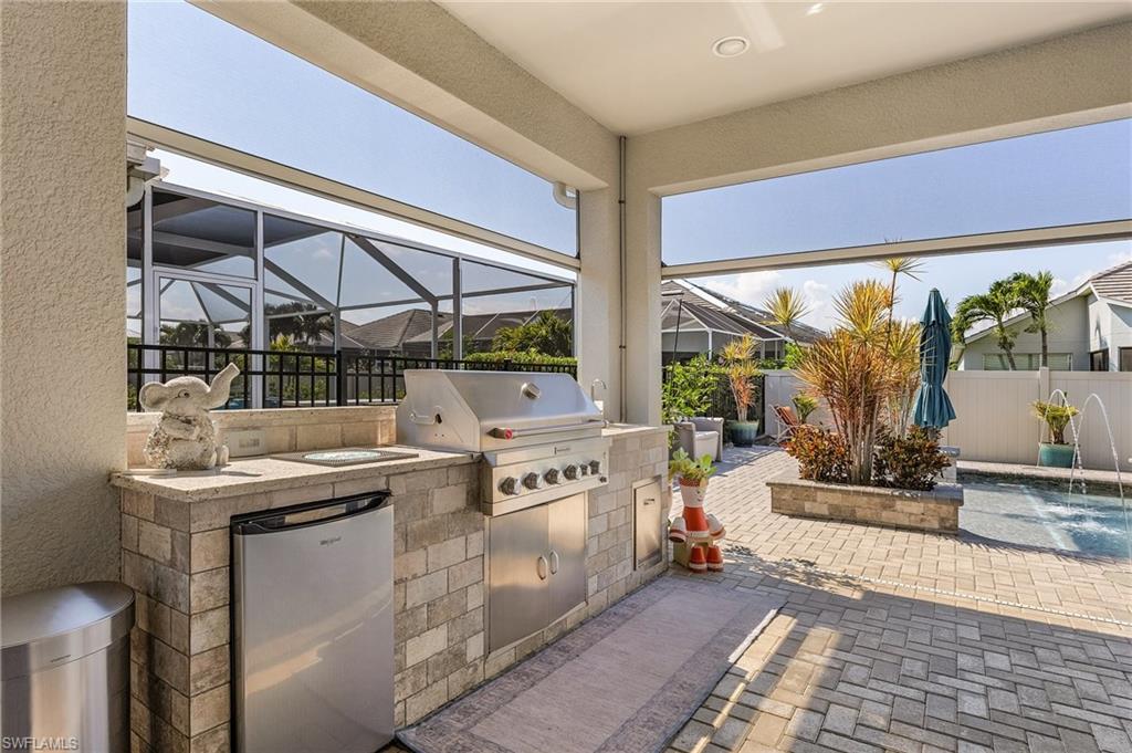 Covered outdoor kitchen featuring a built-in stainless steel grill, integrated mini-refrigerator, and stone-finish countertop