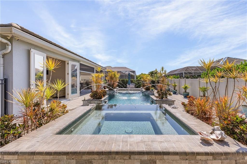 Outdoor pool with integrated spa and water features, surrounded by decorative plantings