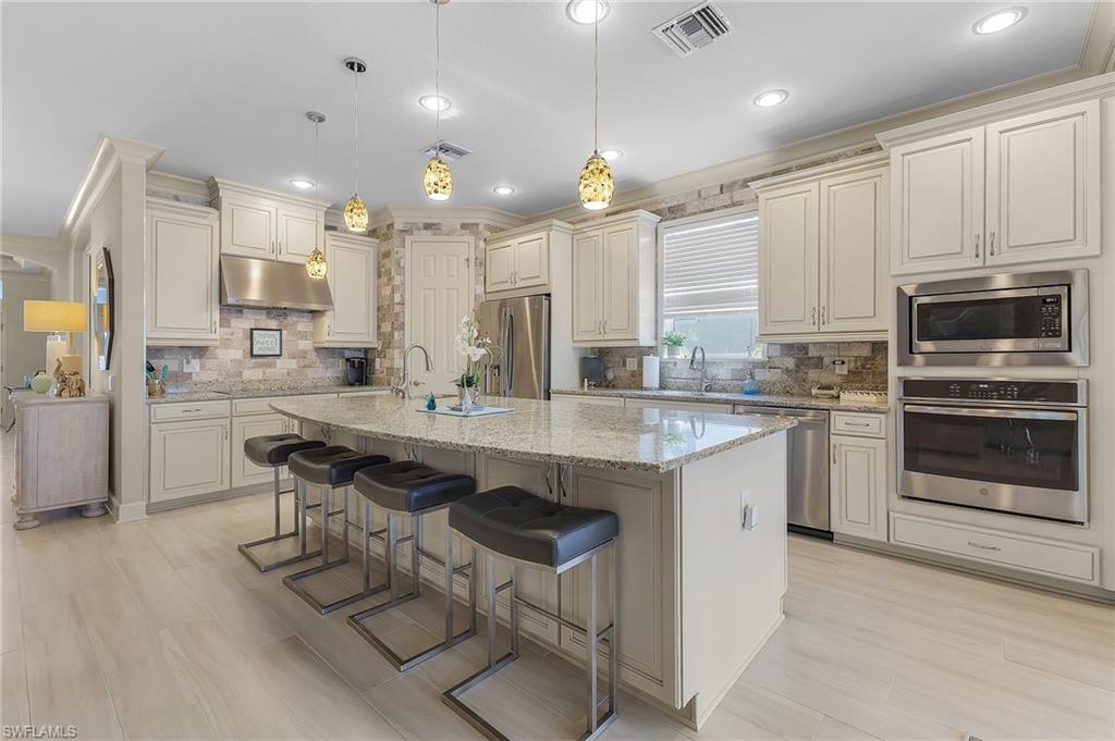 Spacious kitchen featuring an expansive center island with seating, granite countertops, light-toned cabinetry, stainless steel appliances, and wood-finish flooring