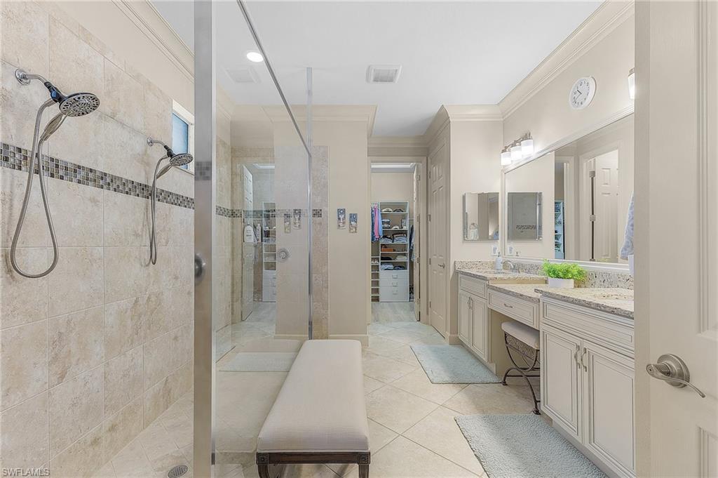 Spacious bathroom featuring a dual vanity with light-colored countertops, large wall-mounted mirror, tiled flooring, and a walk-in shower with dual shower heads and mosaic accent tile