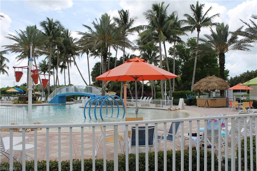 Expansive pool area featuring a bridge, water play structures, a thatched-roof tiki bar, mature palm trees, and ample patio seating