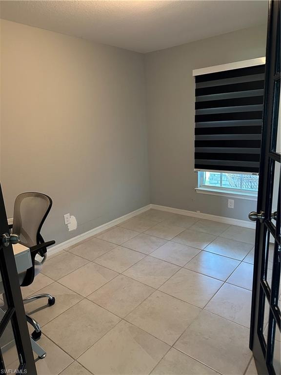 Interior room featuring neutral wall paint, tile flooring, a window with layered shades, and a doorway with French doors