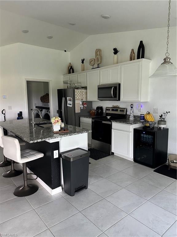 Kitchen featuring a granite-topped island with seating, stainless steel appliances, white cabinetry, and vaulted ceilings