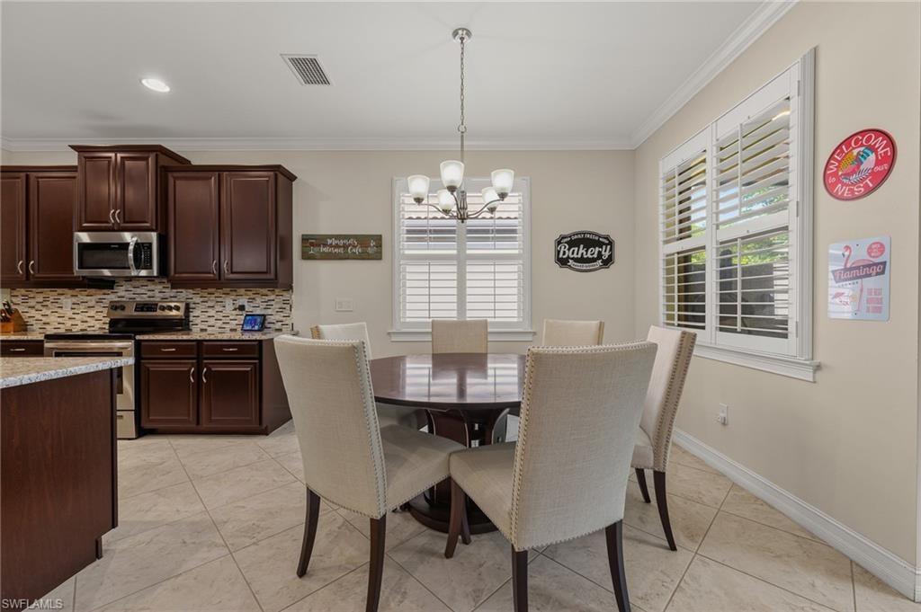 Dining area featuring a circular wood-finish table with upholstered chairs, tiled flooring, plantation shutters, and a chandelier