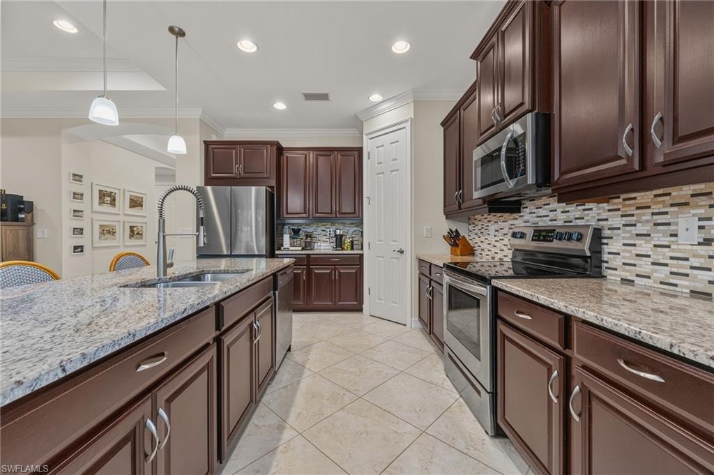 Kitchen featuring a large island with sink, dark wood cabinetry, light-toned granite countertops, stainless steel appliances, and a mosaic tile backsplash