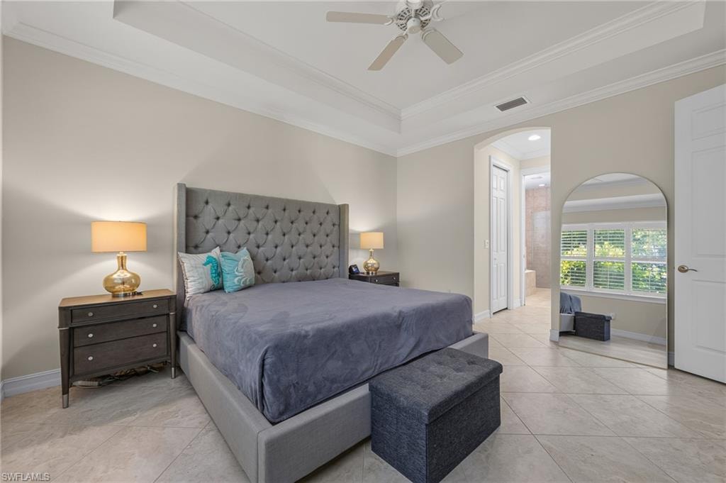 Spacious room featuring tile flooring, a tray ceiling with a ceiling fan, and an arched doorway leading to an additional space