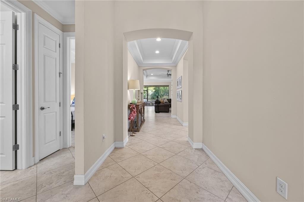Arched entryway leading to an interior hallway with light tile flooring, recessed lighting, and crown molding