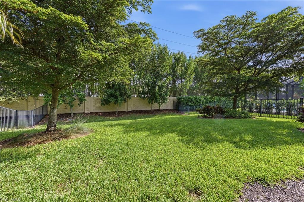 Expansive grassy yard featuring mature trees and a black metal fence