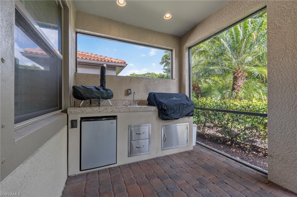 Outdoor kitchen featuring a built-in sink, under-counter refrigerator, stainless steel storage drawers, and durable paver flooring