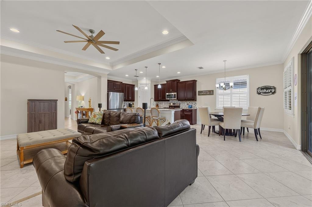 Expansive open-concept living area featuring tray ceilings with recessed lighting, an oversized ceiling fan, and large format tile flooring