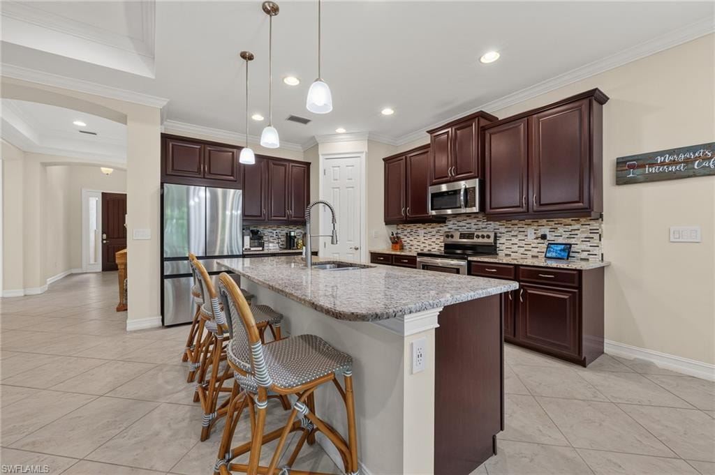 Kitchen featuring dark wood cabinetry, stainless steel appliances, a tile backsplash, and a large central island with a light-toned countertop