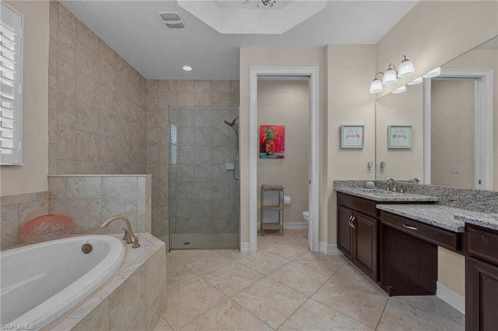 Spacious bathroom featuring a built-in soaking tub with deck-mounted brushed nickel fixtures, a separate glass-enclosed shower, a double vanity with granite countertops and dark wood cabinetry, and tiled flooring
