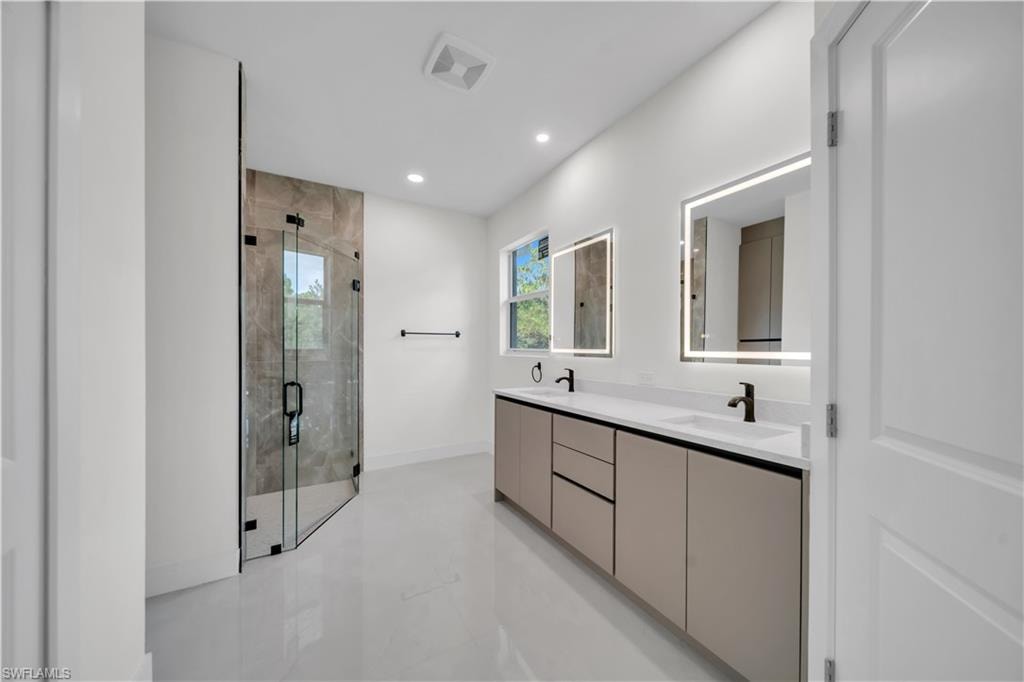 Master bathroom featuring a glass-enclosed shower with tile surround, a dual vanity with undermount sinks and matte black faucets, dual back-lit mirrors, and large format floor tile