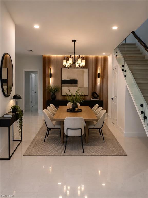 (AI Staged) Dining area featuring a wood-slat accent wall with integrated sconces, a contemporary chandelier, and recessed lighting