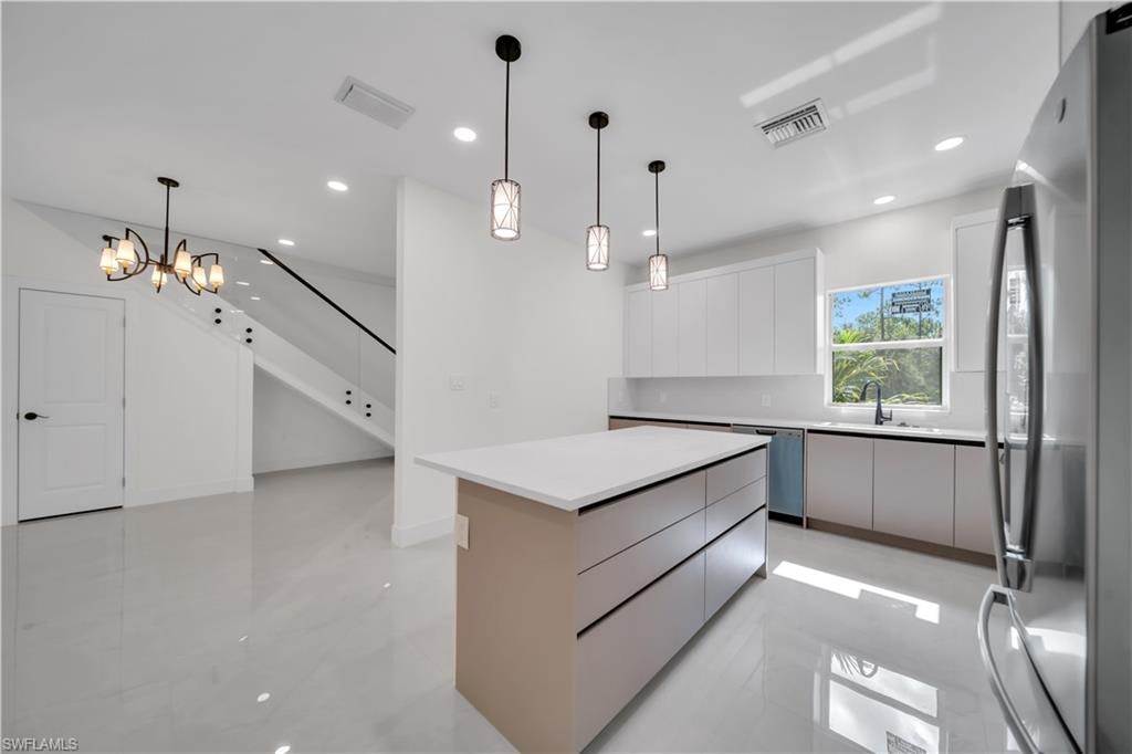 Sleek kitchen featuring a central island with countertop space and integrated drawers, white flat-panel cabinetry, stainless steel appliances, and a black gooseneck faucet