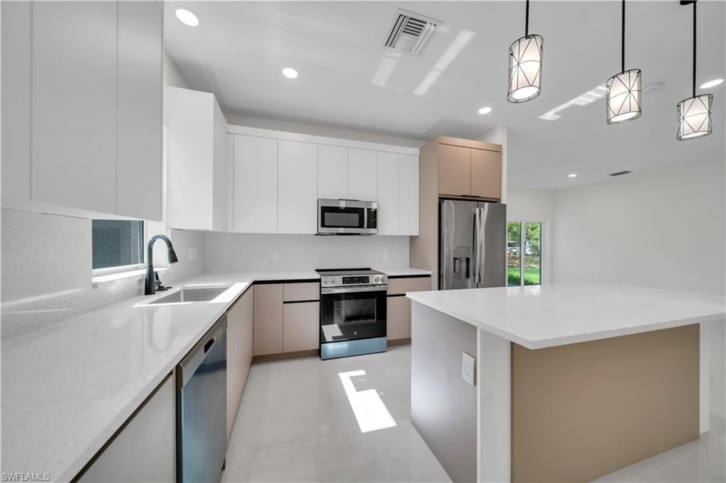 Modern kitchen featuring white and tan cabinetry with sleek hardware, stainless steel appliances, and recessed lighting
