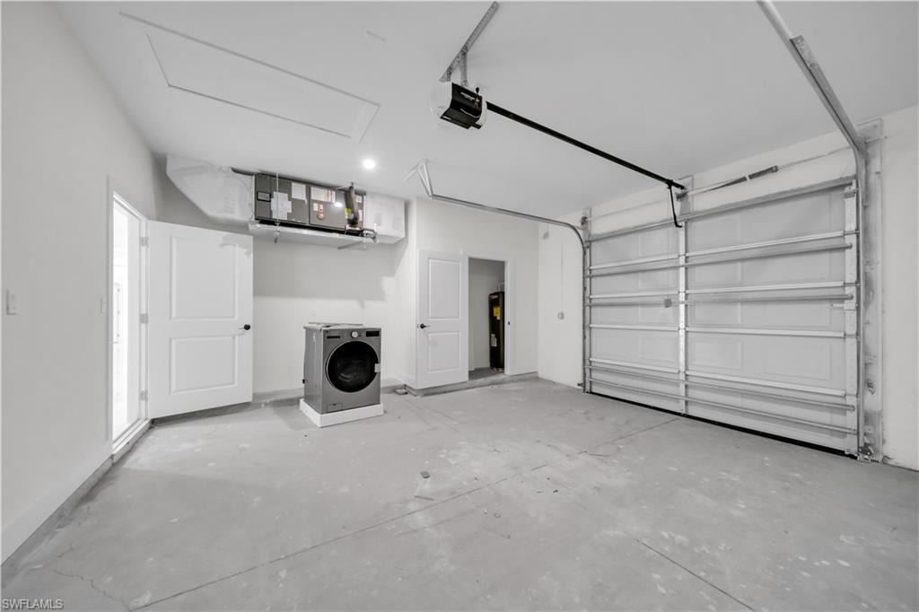 Spacious garage featuring a concrete floor, overhead garage door, built-in air handler, and a side access door