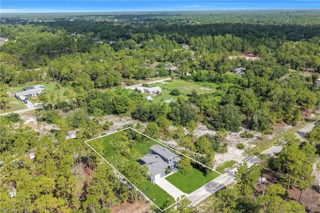 Aerial view showcasing a property with a manicured green lawn, mature trees, and a paved driveway, surrounded by extensive natural landscaping